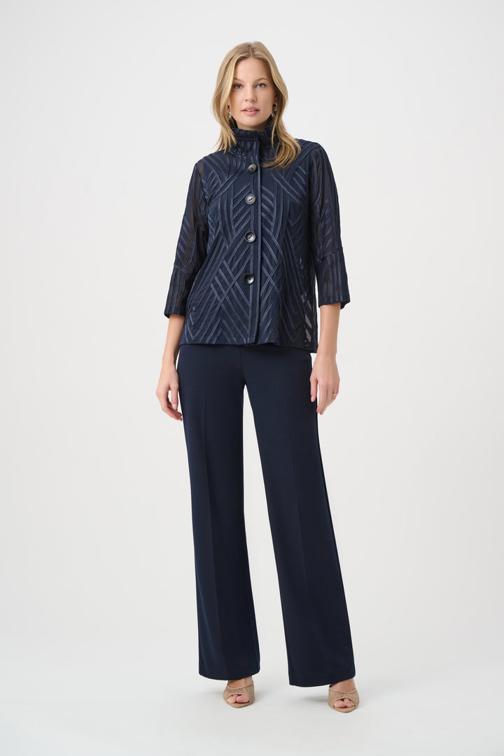 A woman modelling a navy textured jacket with navy pants standing in front of a grey background. 