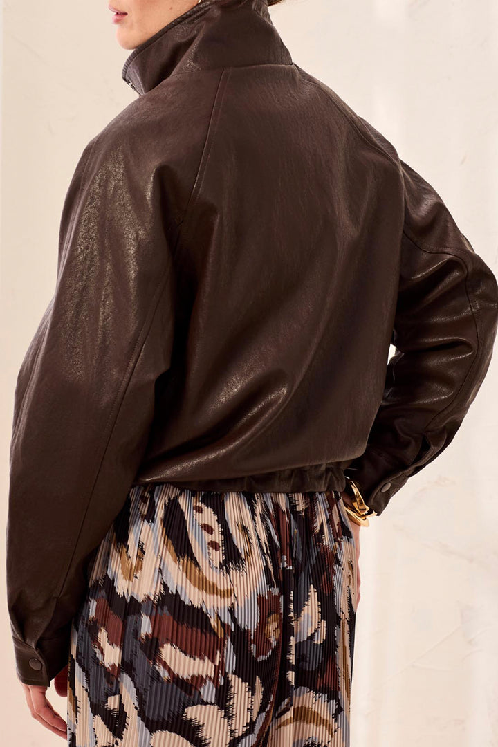 A woman shown from the back wearing a faux leather bomber style brown jacket standing in front of a beige background. 