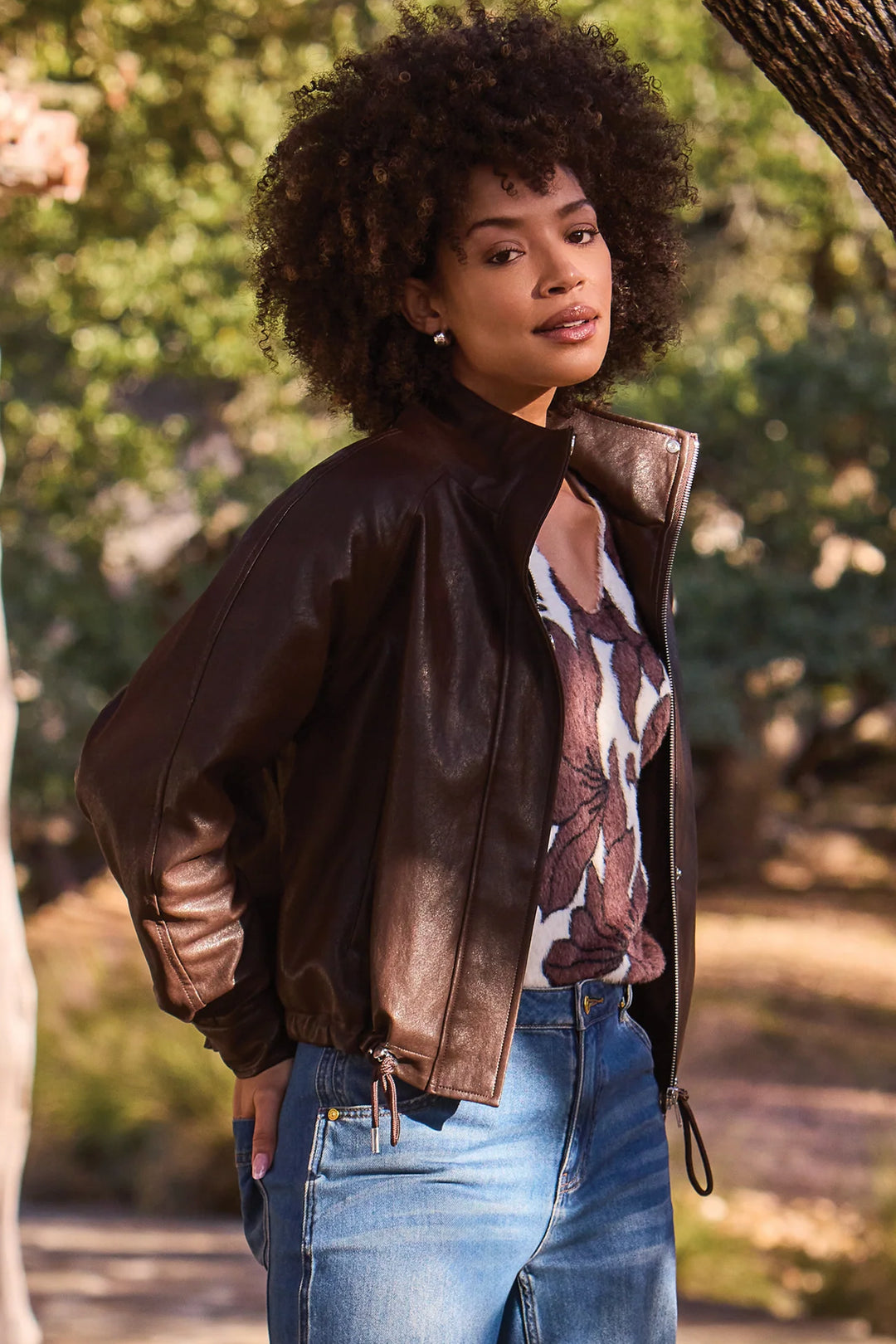 A woman wearing a faux leather bomber style brown jacket.