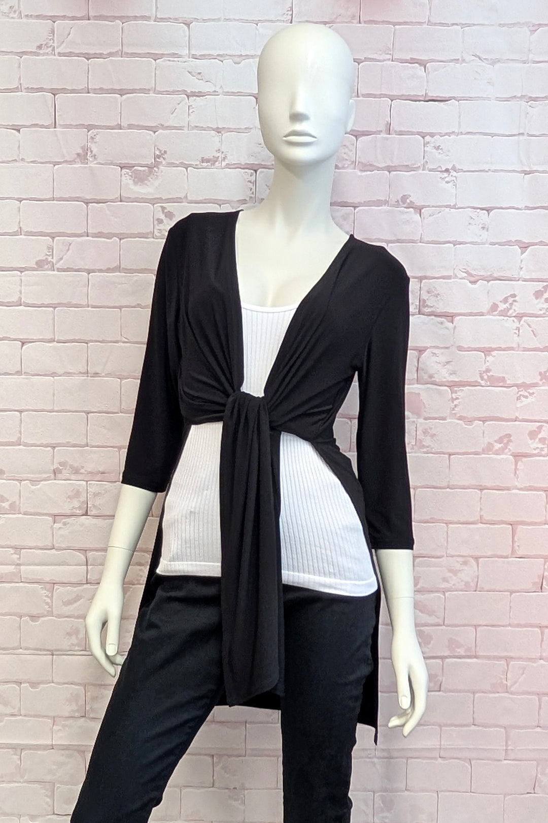 Mannequin wearing a black cardigan over a white top and black pants against a light brick wall.