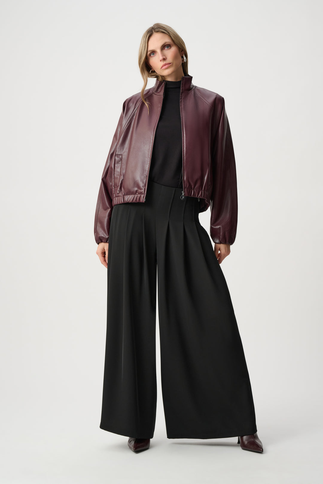 Woman wearing a burgundy leather jacket and black pants on a white background