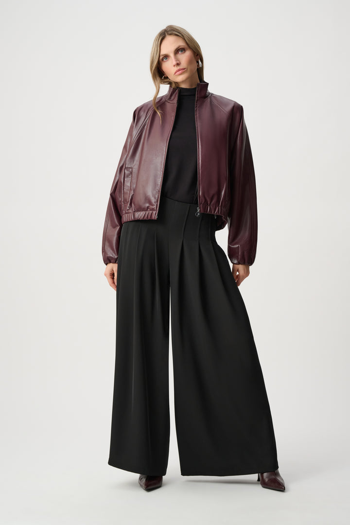 Woman wearing a burgundy leather jacket and black pants on a white background