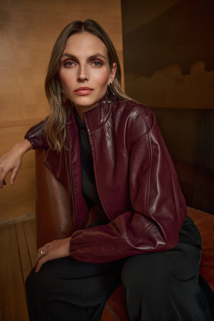 Woman wearing a burgundy leather jacket sitting on a wooden bench.