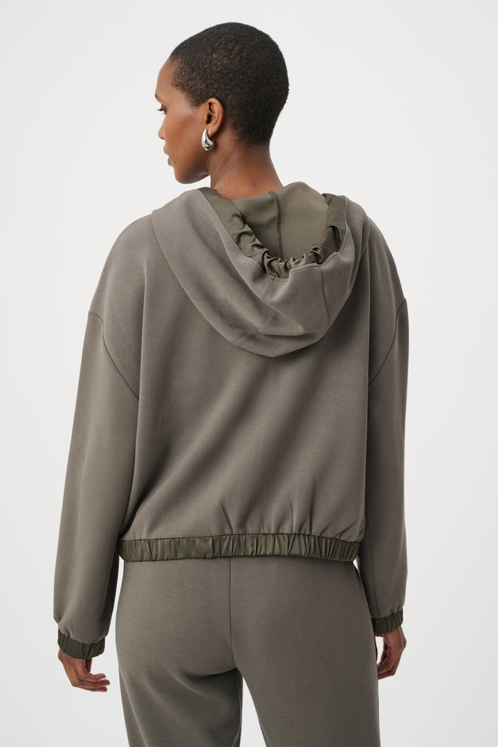A woman shown from the back standing in from of a light grey background wearing an olive coloured satin trim hoodie jacket and matching pants. 