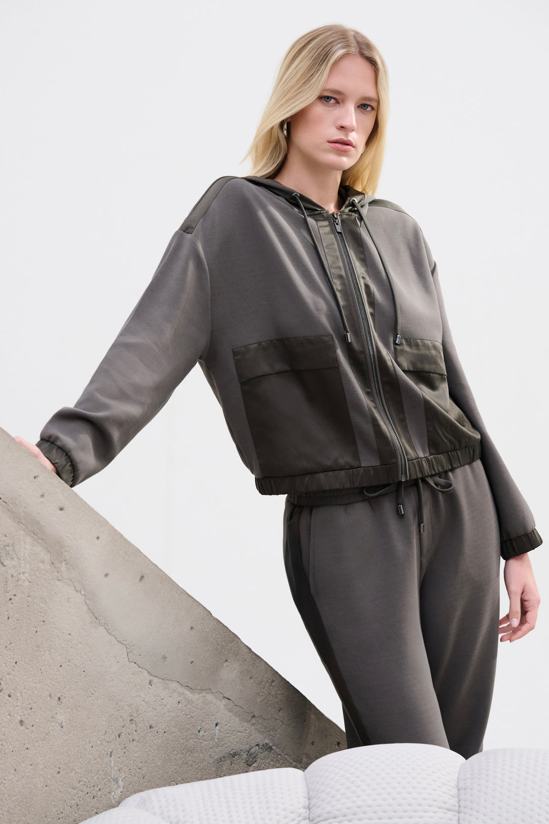 A woman wearing an olive coloured satin trim hoodie jacket and matching pants. 
