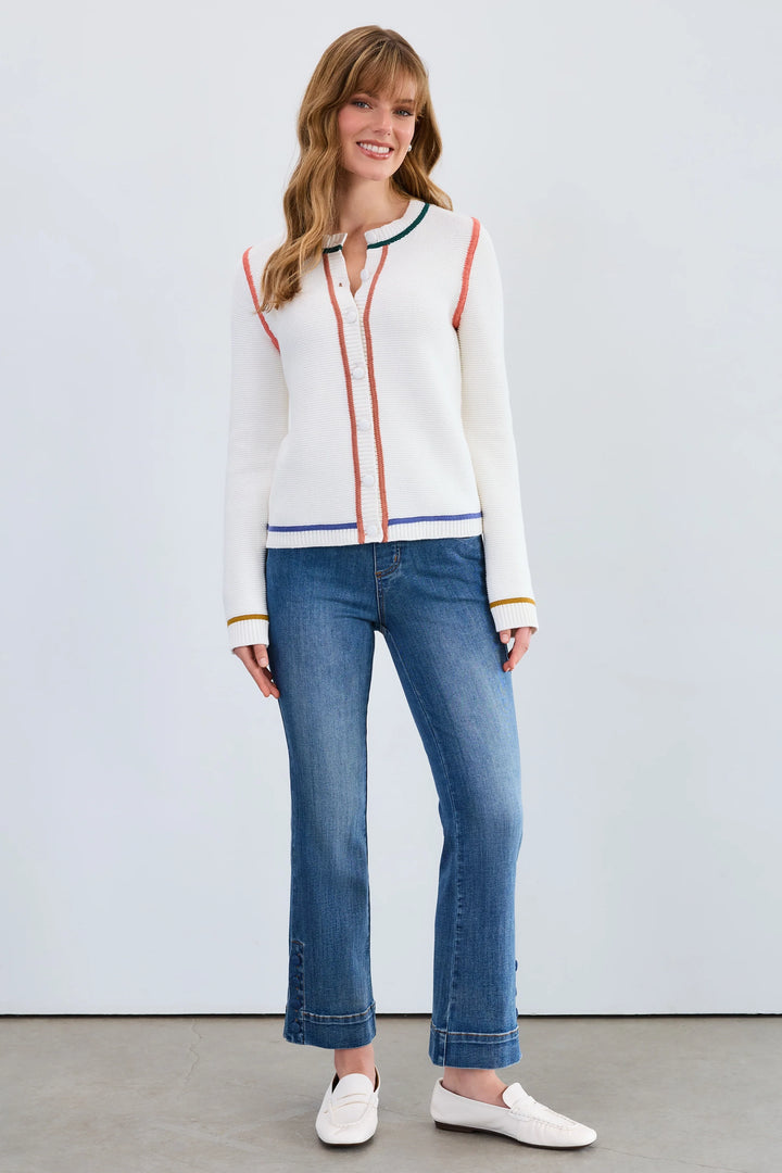 Woman wearing a white sweater with colorful accents and blue jeans on a plain background