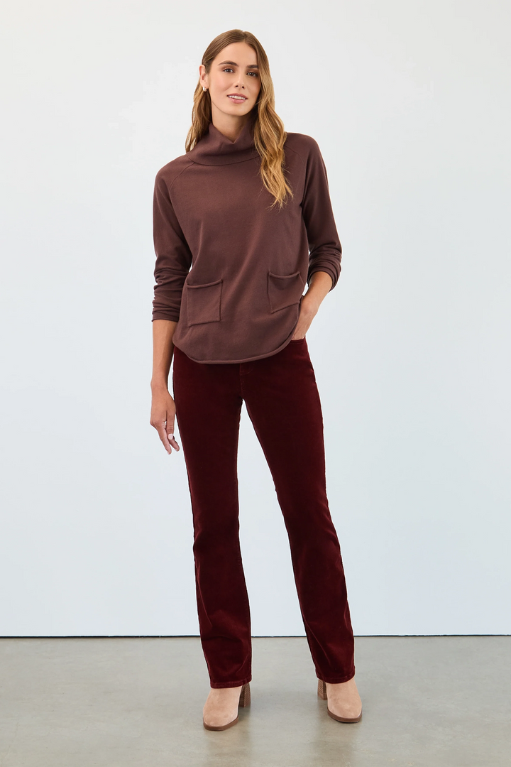 Woman wearing a brown turtleneck top and burgundy pants against a white background