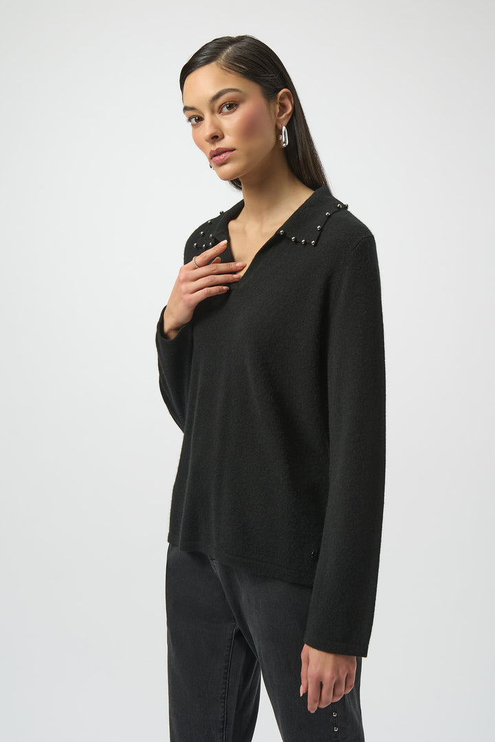 Woman wearing a black long-sleeve sweater top with embellishments on a white background