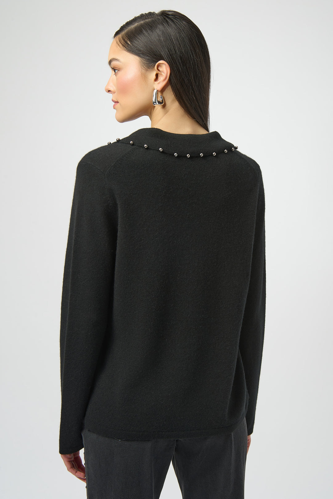 Black sweater with decorative elements on the collar on the back worn by a person against a white background