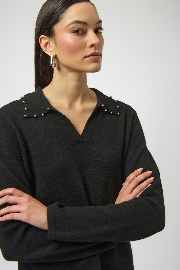 Woman wearing a black sweater top with studded details on a plain background