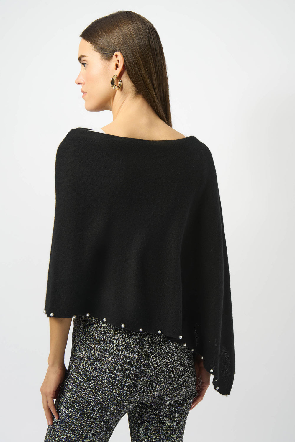 Woman wearing a black poncho with pearl embellishments on a white background