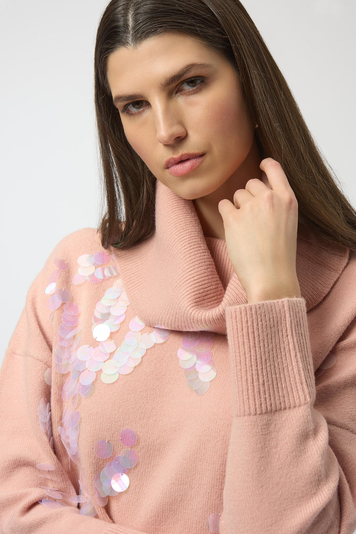 Woman wearing a pink sweater with sequin details on a plain background