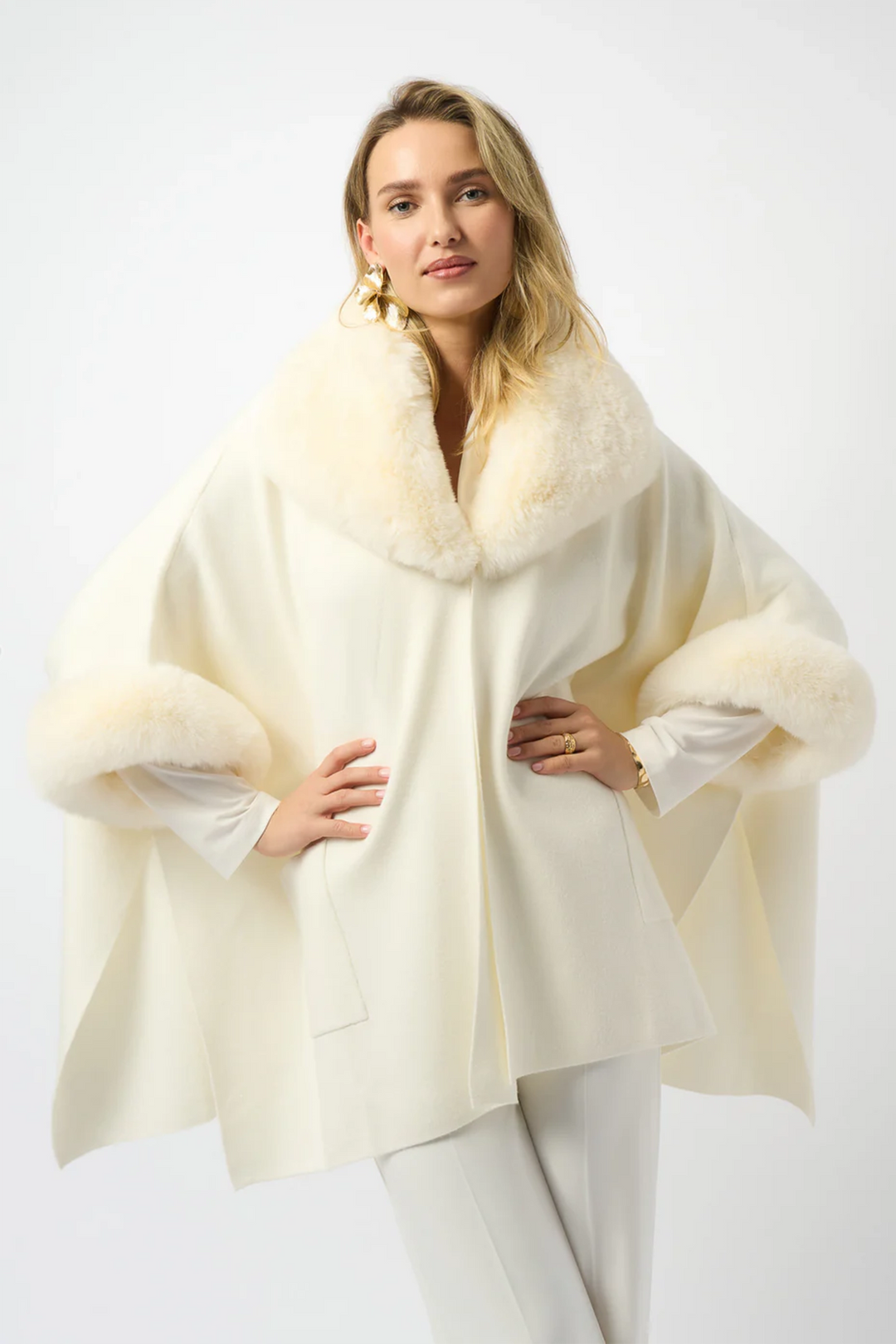 Woman wearing a cream-colored cape with faux fur trim on a white background