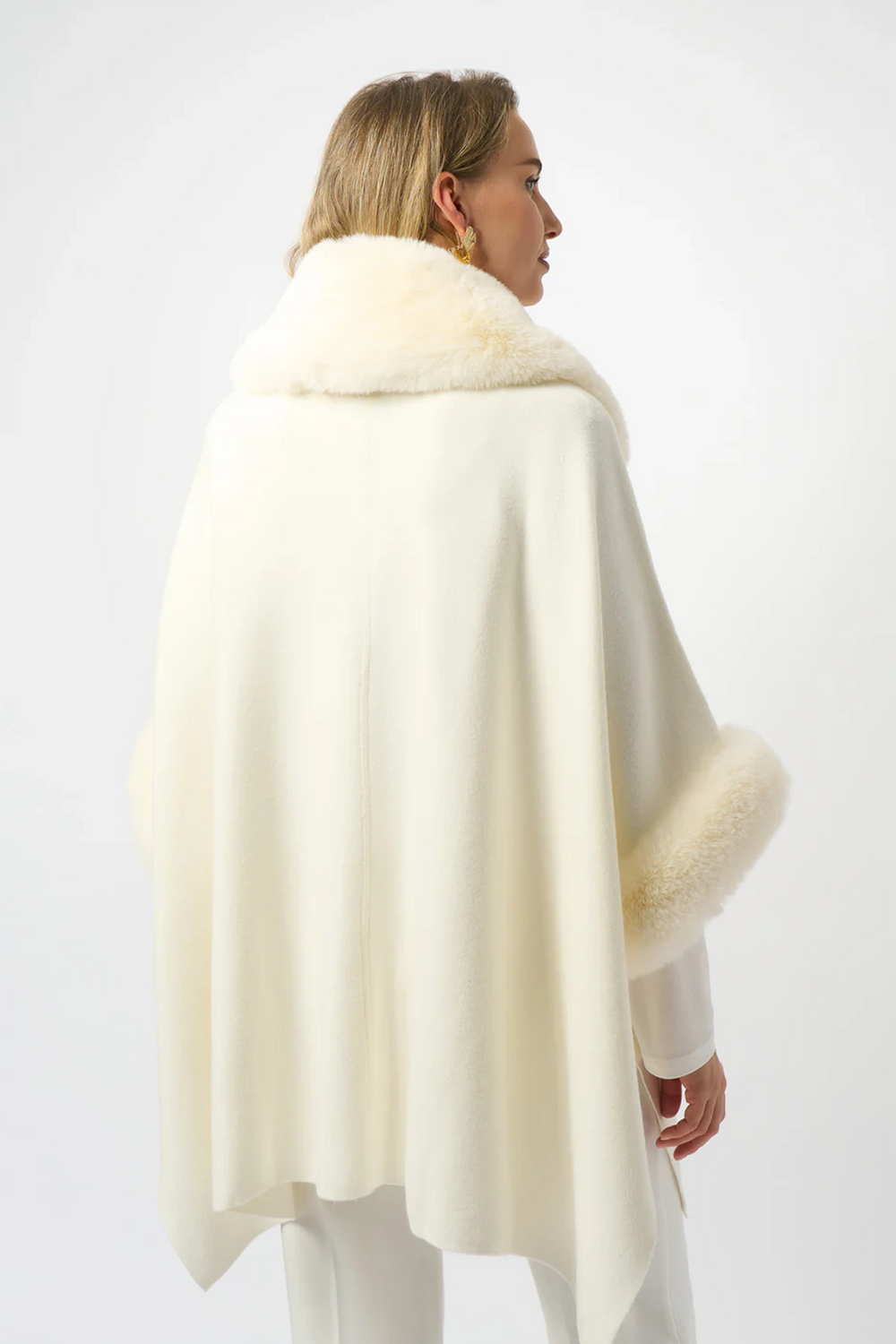 Woman wearing a cream-colored cape with faux fur trim on a white background