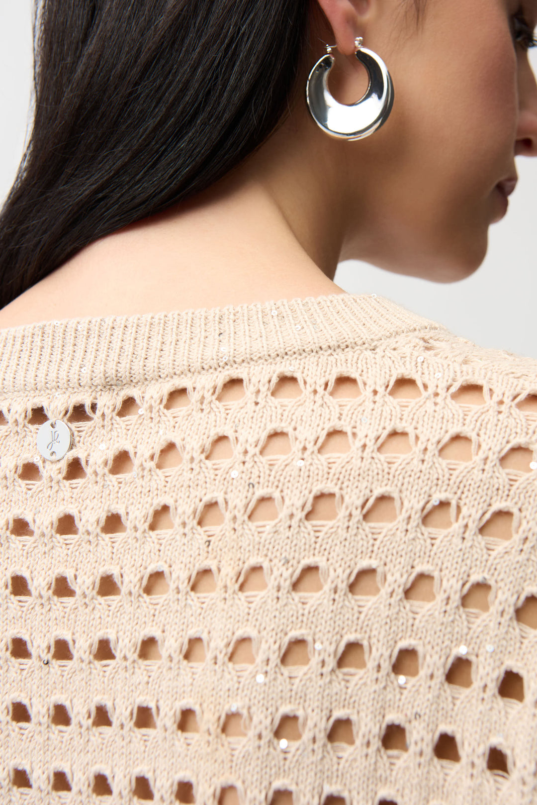 Close-up of a person wearing a beige open-knit cardigan and silver hoop earrings.