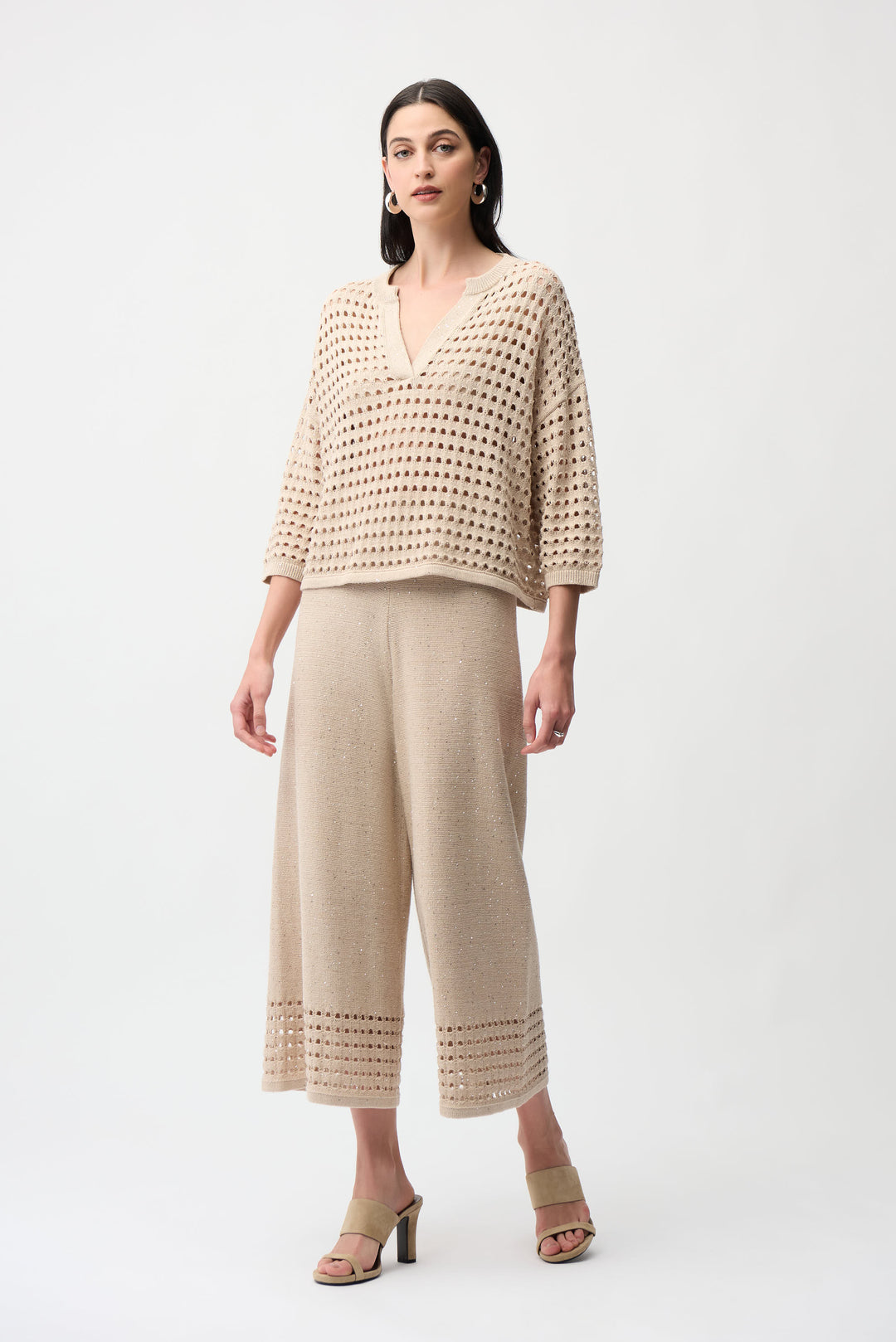 Woman wearing a beige crochet sweater top and wide-leg pants on a white background