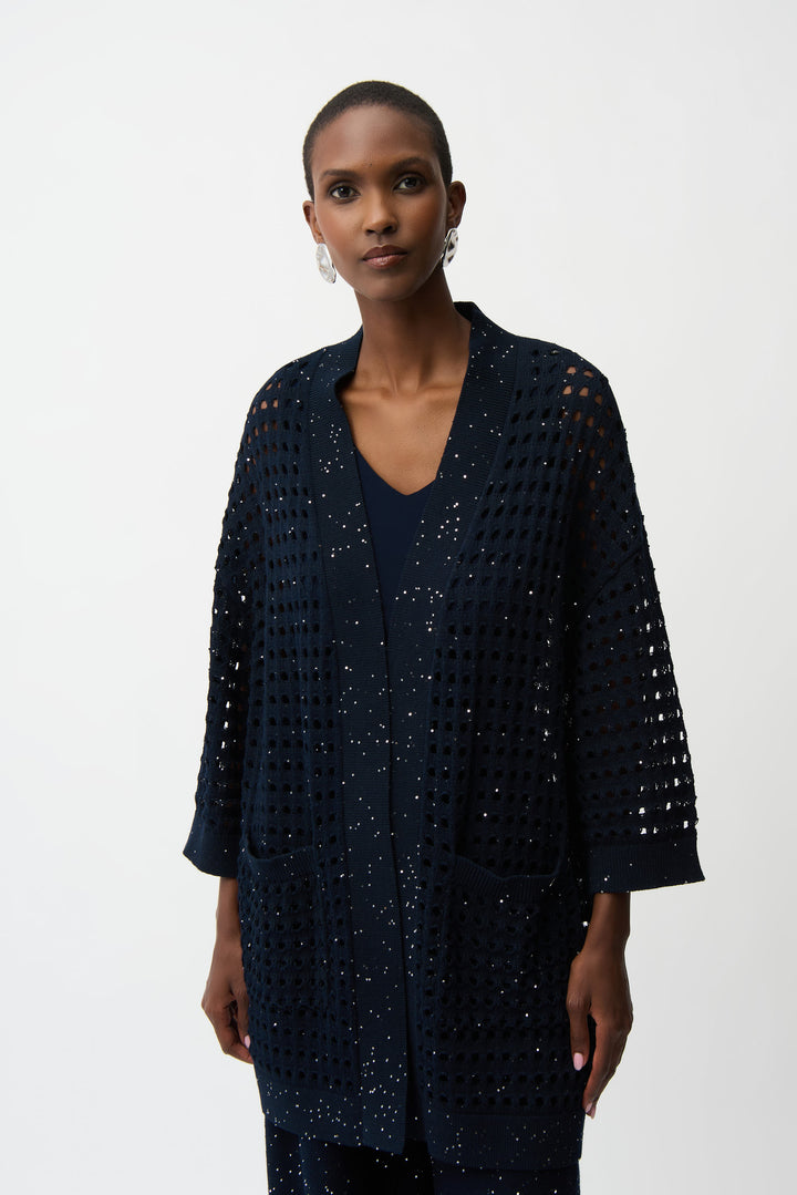 Woman wearing a dark blue textured, crochet open cardigan with a white background