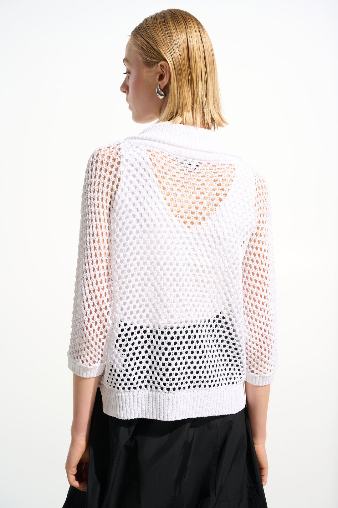 Woman wearing a white mesh cardigan top with crochet knit pattern on a white background