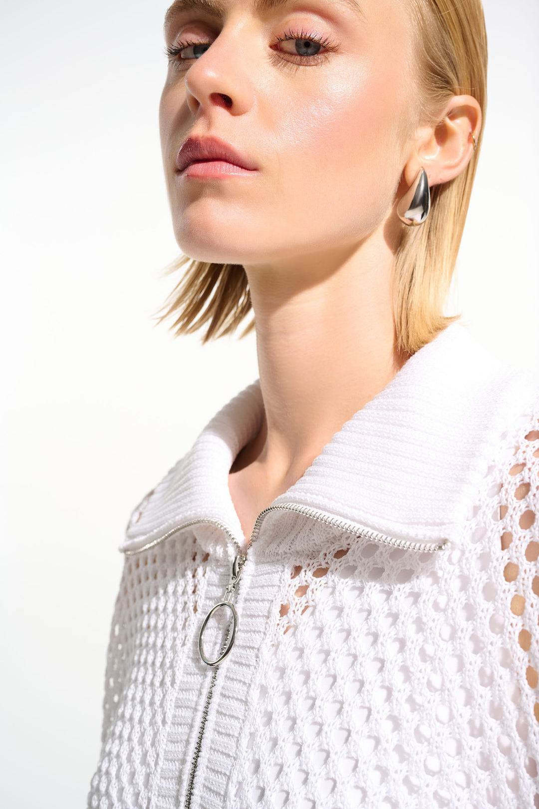 Close-up of a person wearing a white zipper cardigan top with a neutral background