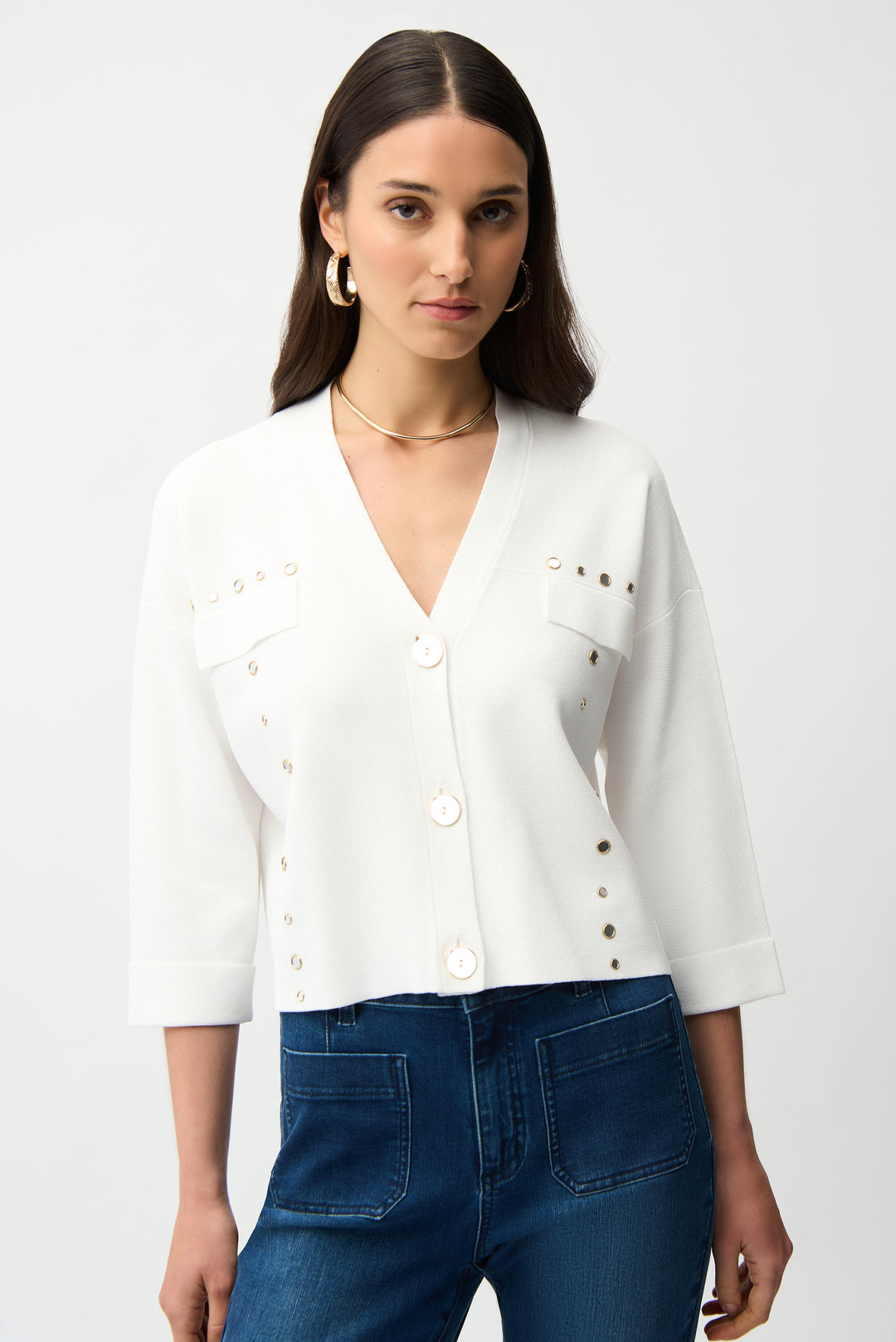 Woman wearing a white button cardigan with jewel details and blue jeans on a white background