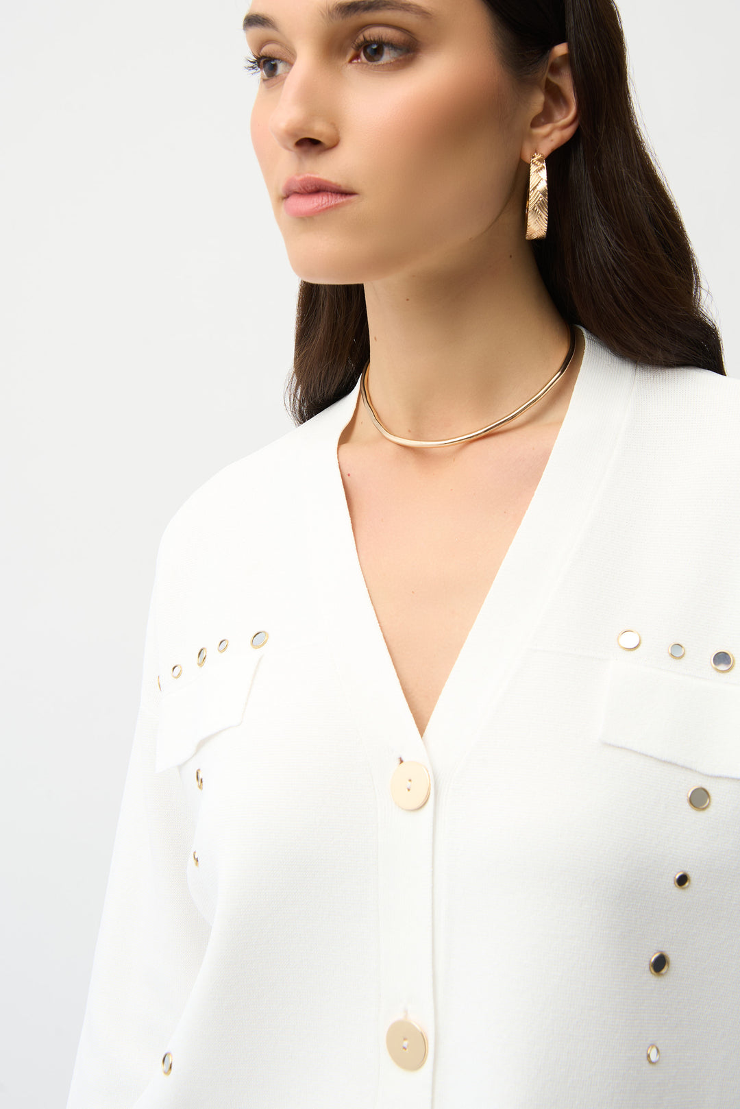 Woman wearing a white button cardigan with gold buttons and gold jewelry against a white background
