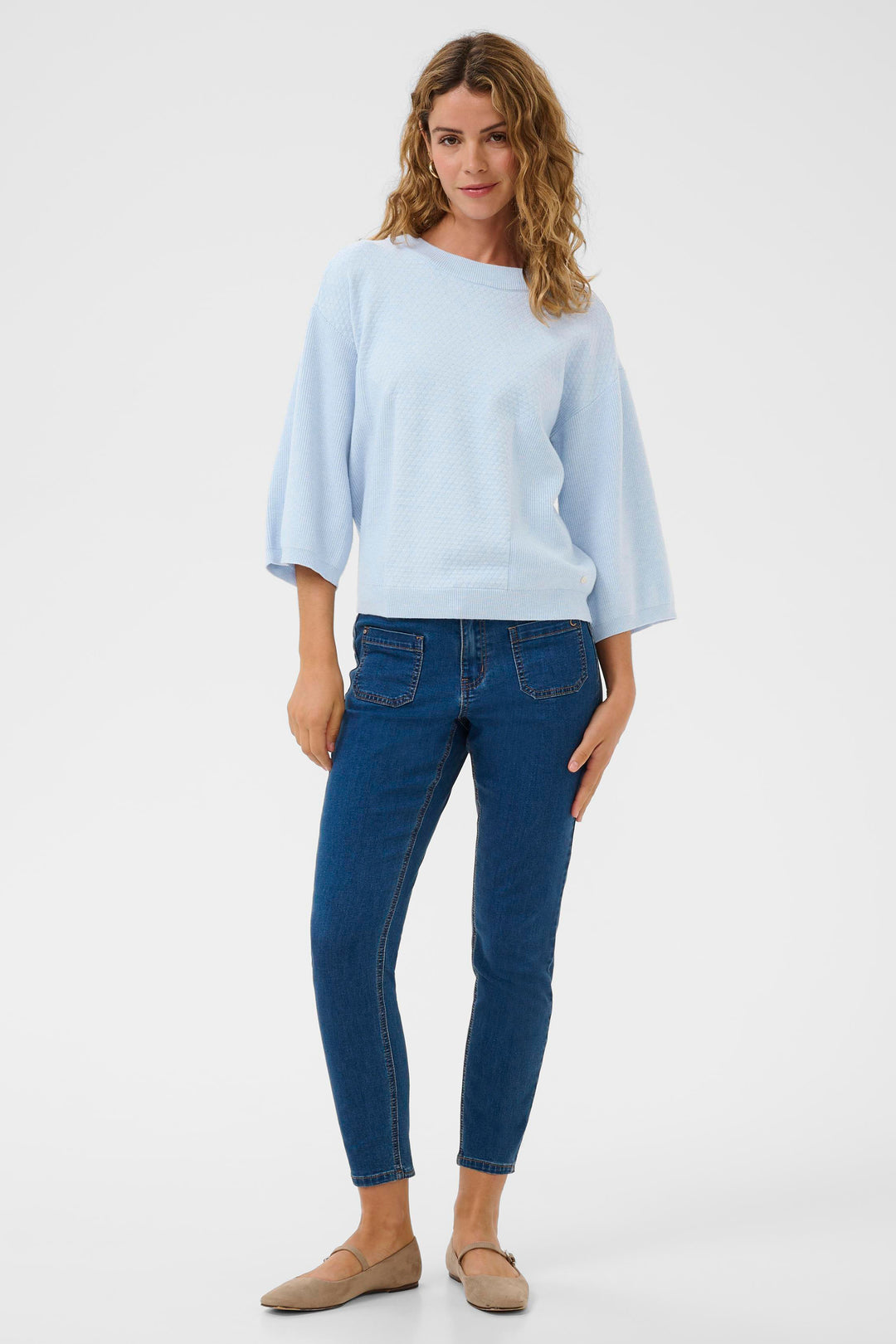 Woman wearing a light blue top and dark blue jeans on a white background