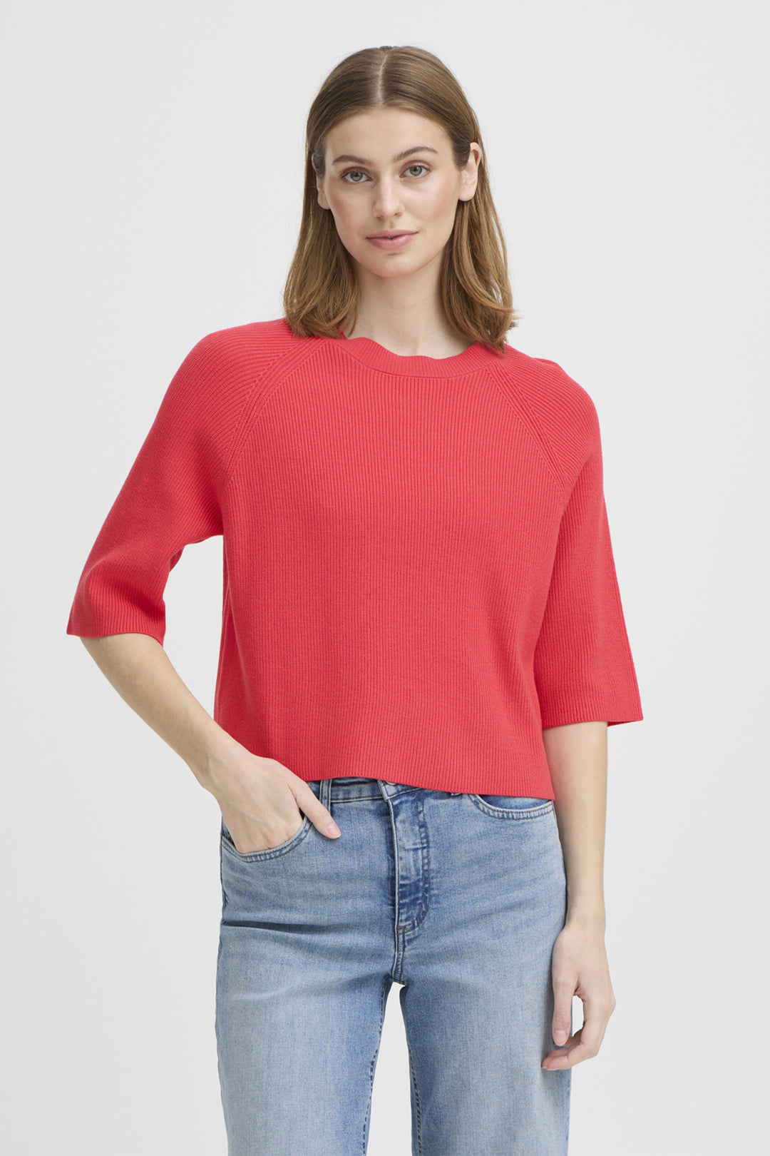 Woman wearing a red sweater and blue jeans on a light gray background
