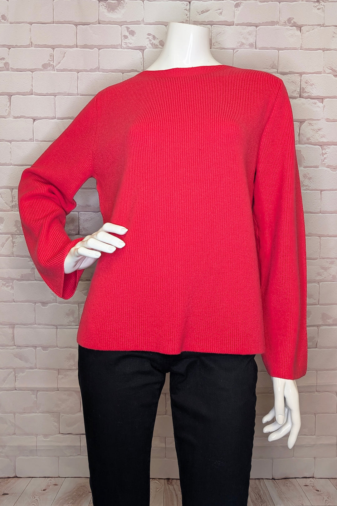 Red sweater on a mannequin against a brick wall.