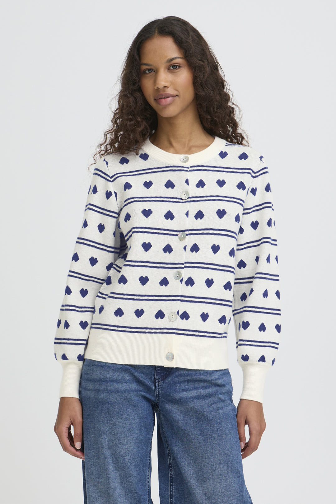 Woman wearing a white sweater with blue pattern and blue jeans on a light gray background