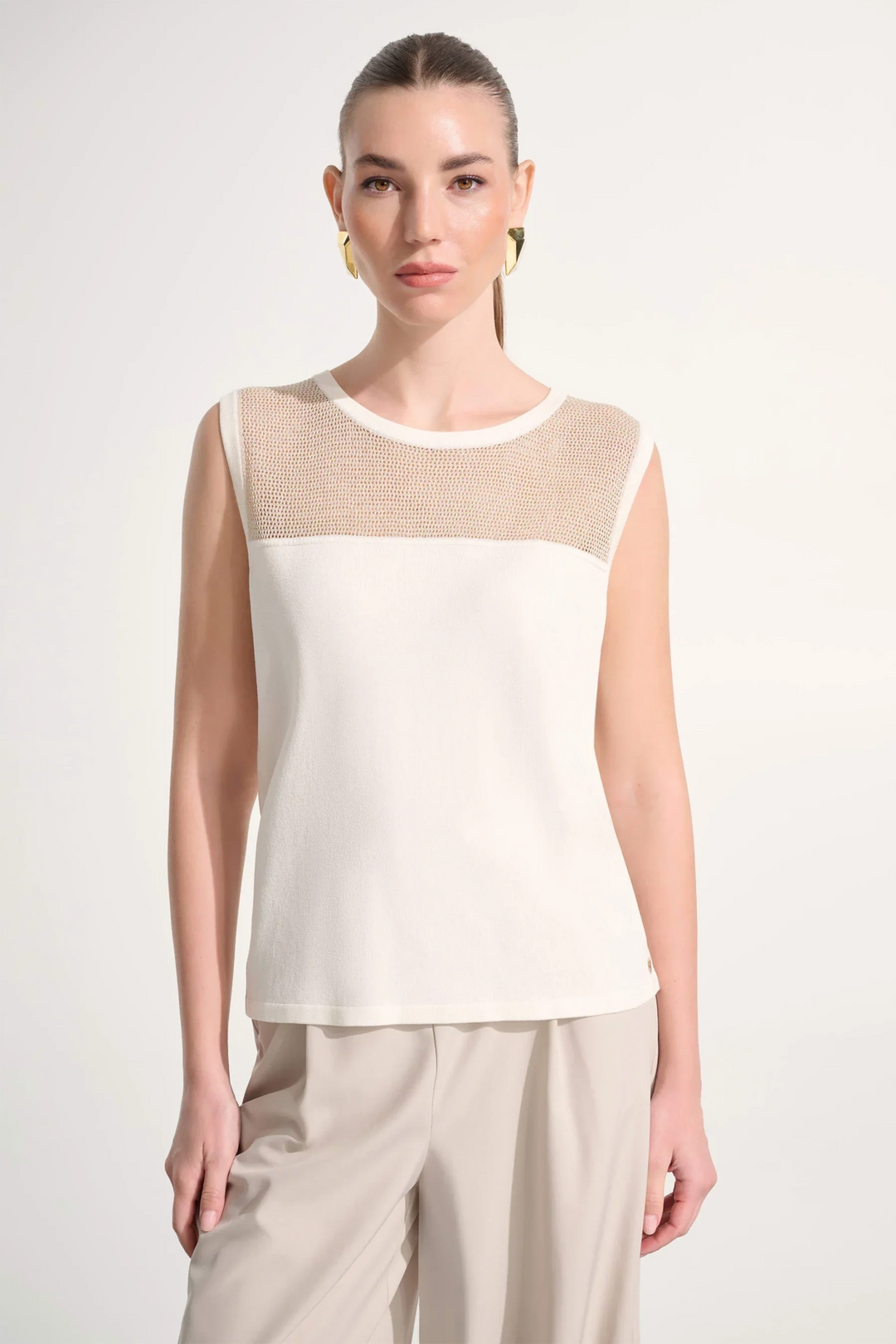 Woman wearing a sleeveless top with beige and white design on a plain background
