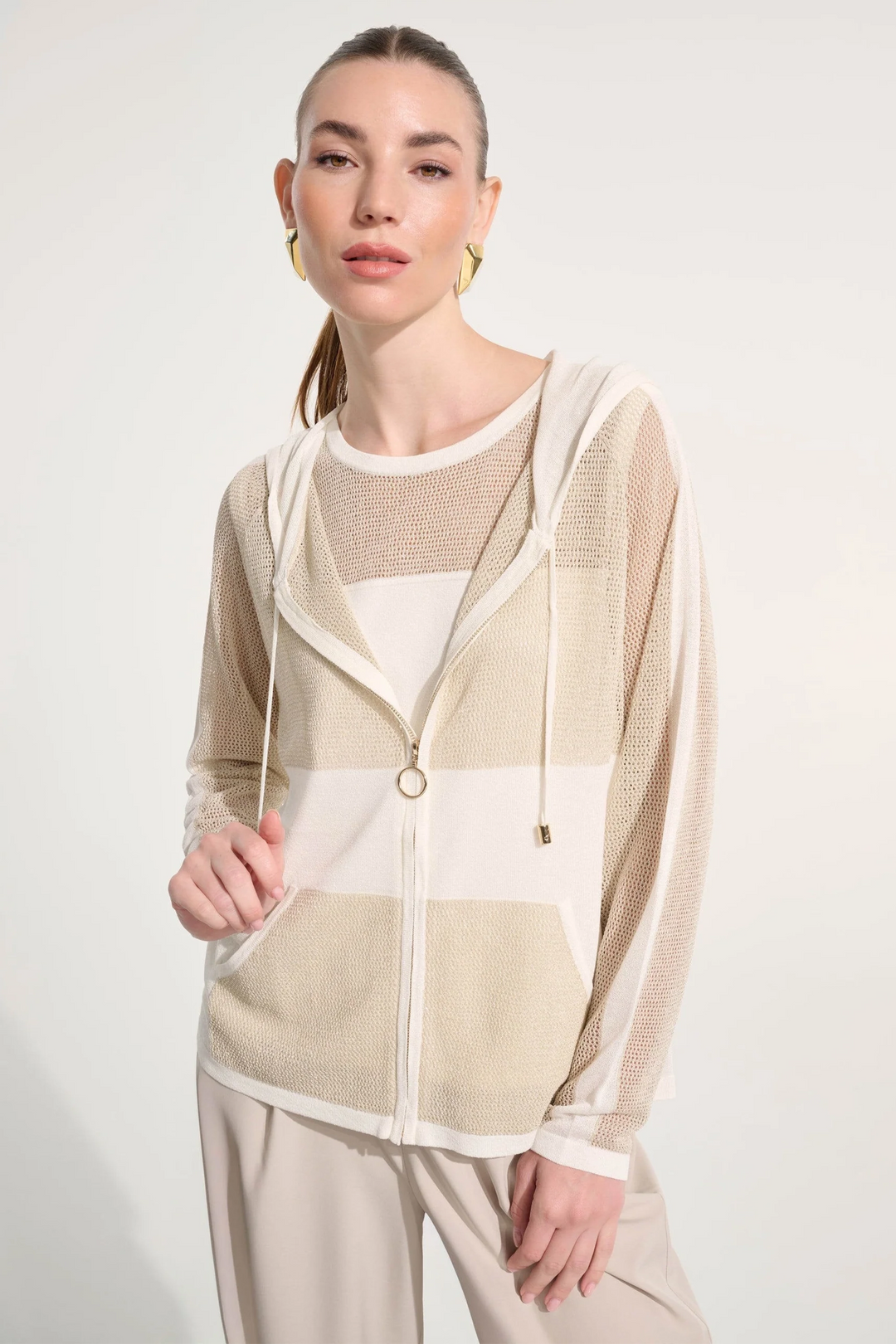 Woman wearing a beige and white striped hoodie cardigan over a white top on a plain background
