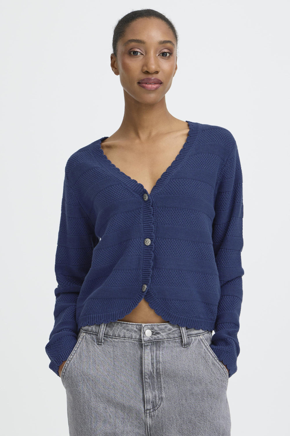 Woman wearing a blue cardigan and gray pants on a white background