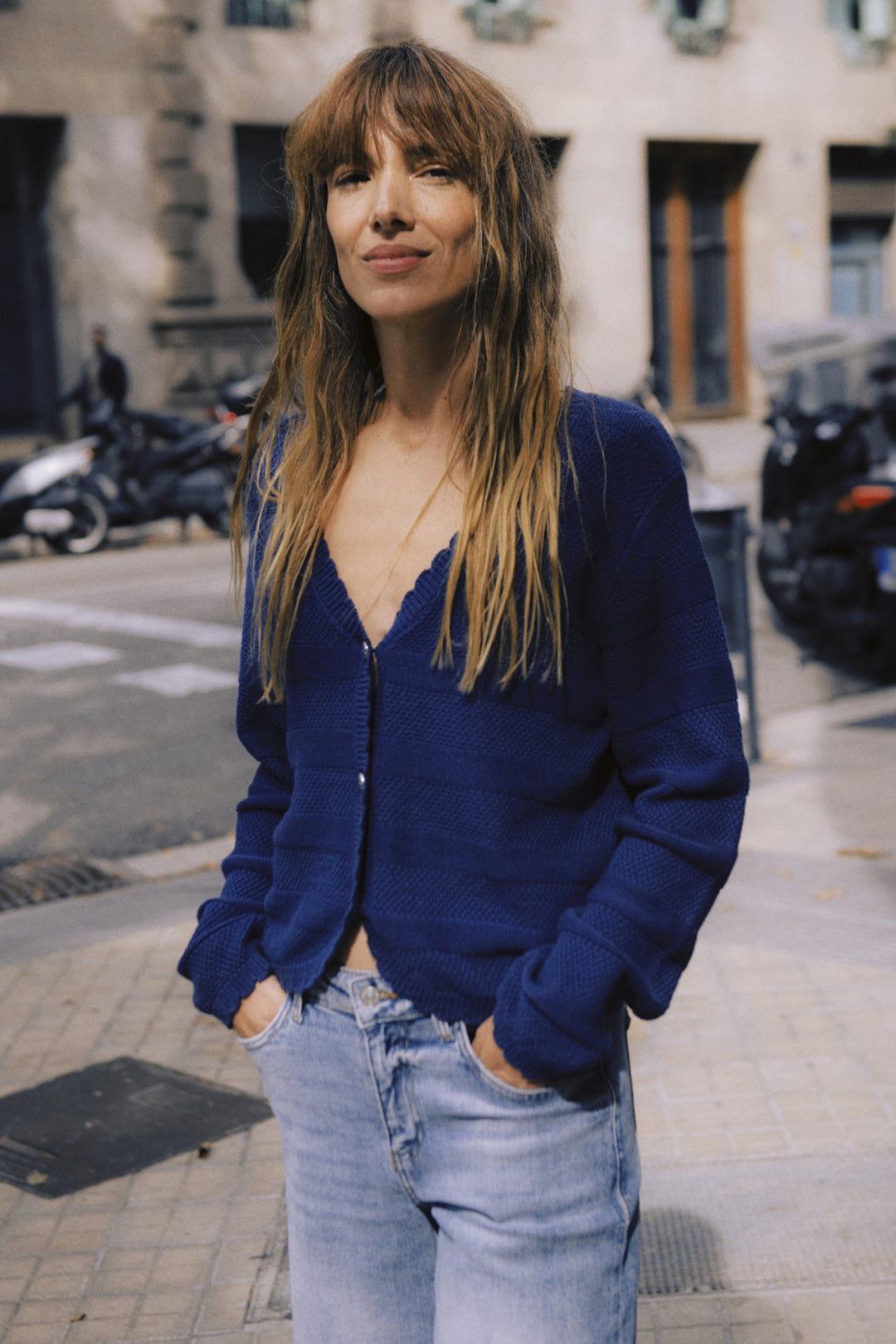 Woman wearing a blue cardigan and jeans standing on a street.