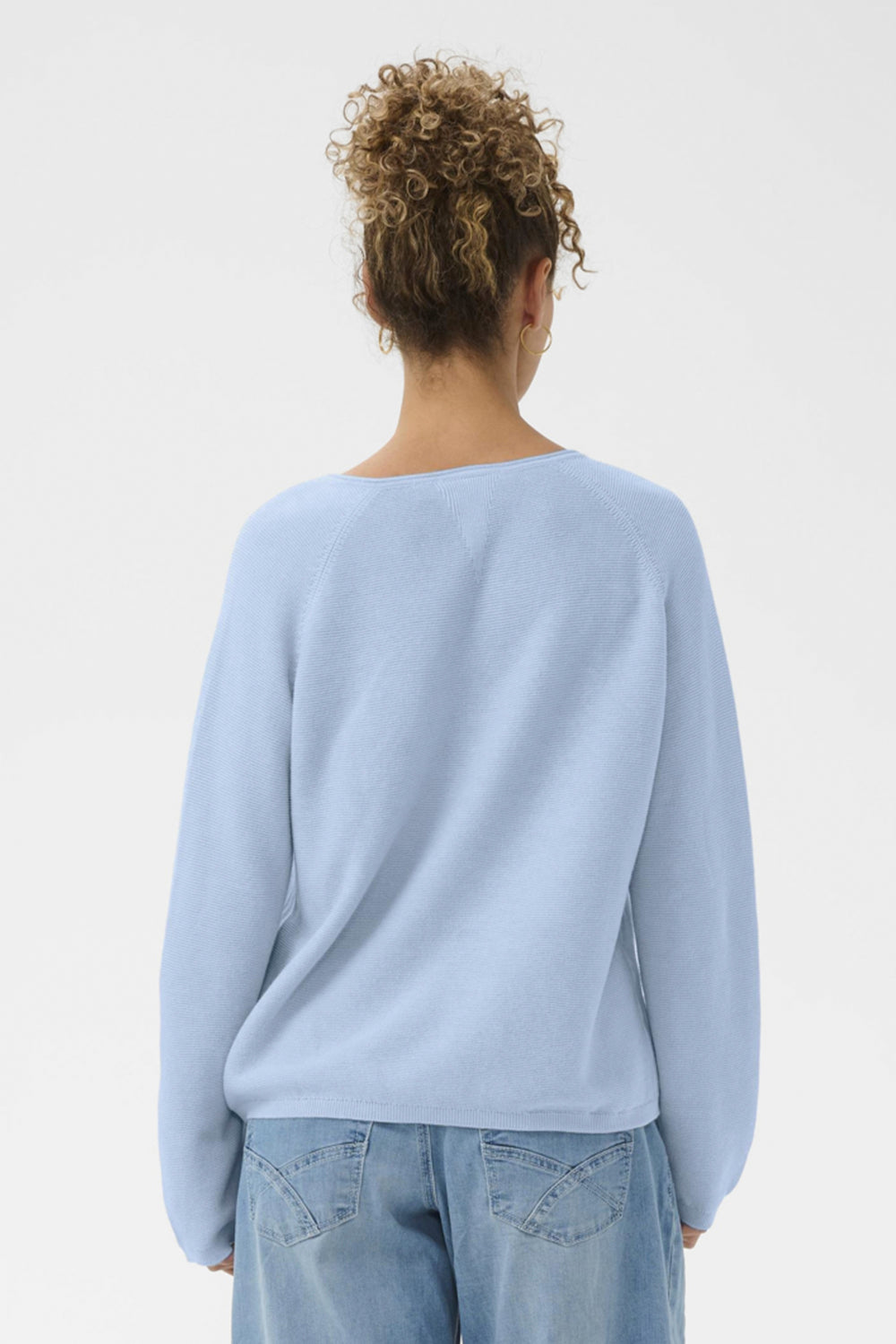 Person wearing a light blue sweater and jeans on a plain background