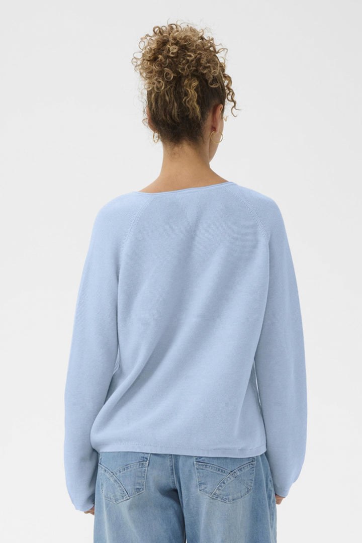 Person wearing a light blue sweater and jeans on a plain background