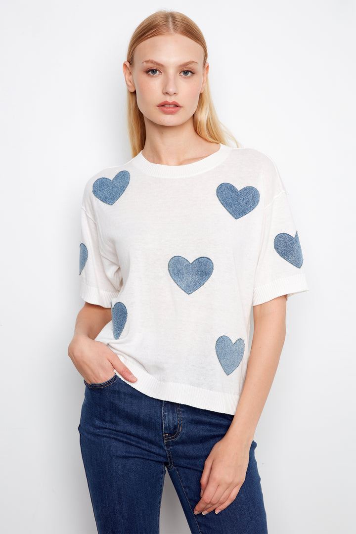 Woman wearing a white sweater with blue heart patterns and blue jeans on a white background