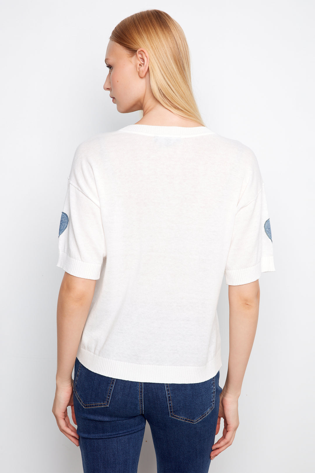 Person wearing a white t-shirt with blue designs on a plain background