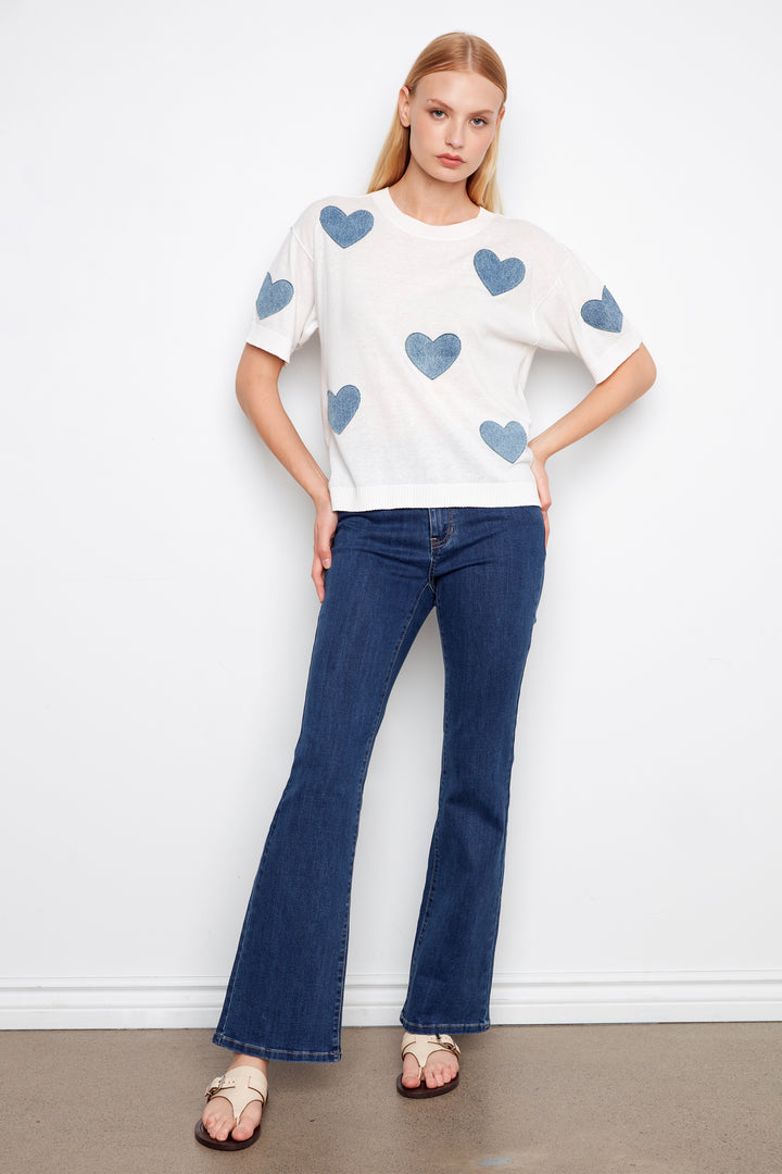 Woman wearing a white t-shirt with blue heart patterns and blue jeans against a white background