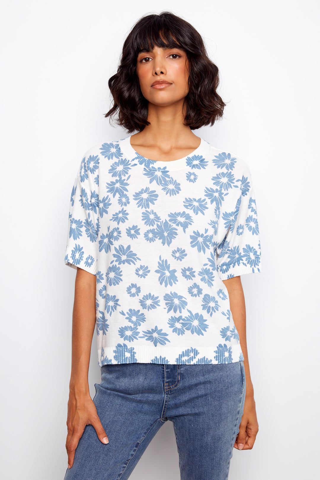 Woman wearing a white light sweater  with blue floral pattern and blue jeans on a white background