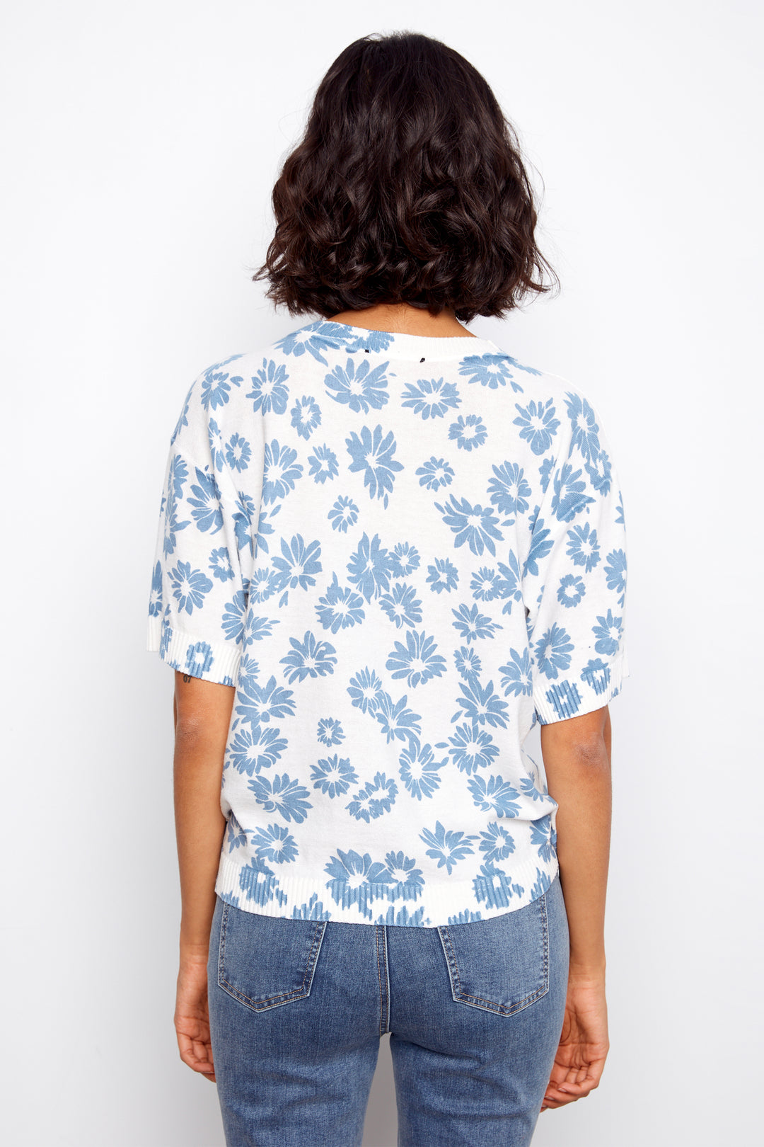 Person wearing a blue floral sweater and jeans on a white background