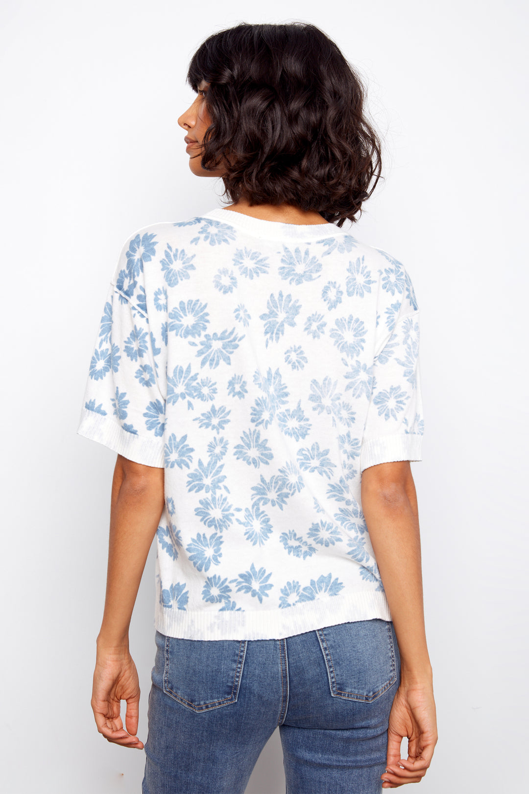 Person wearing a white sweater with blue floral pattern and blue jeans on a white background