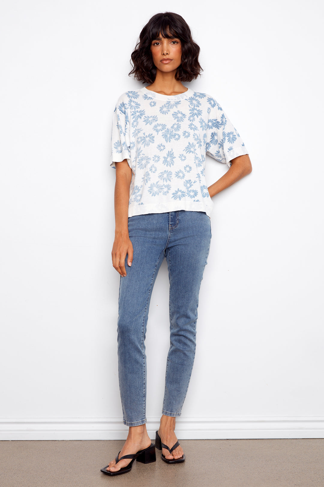 Woman wearing a white floral sweater and blue jeans against a white background