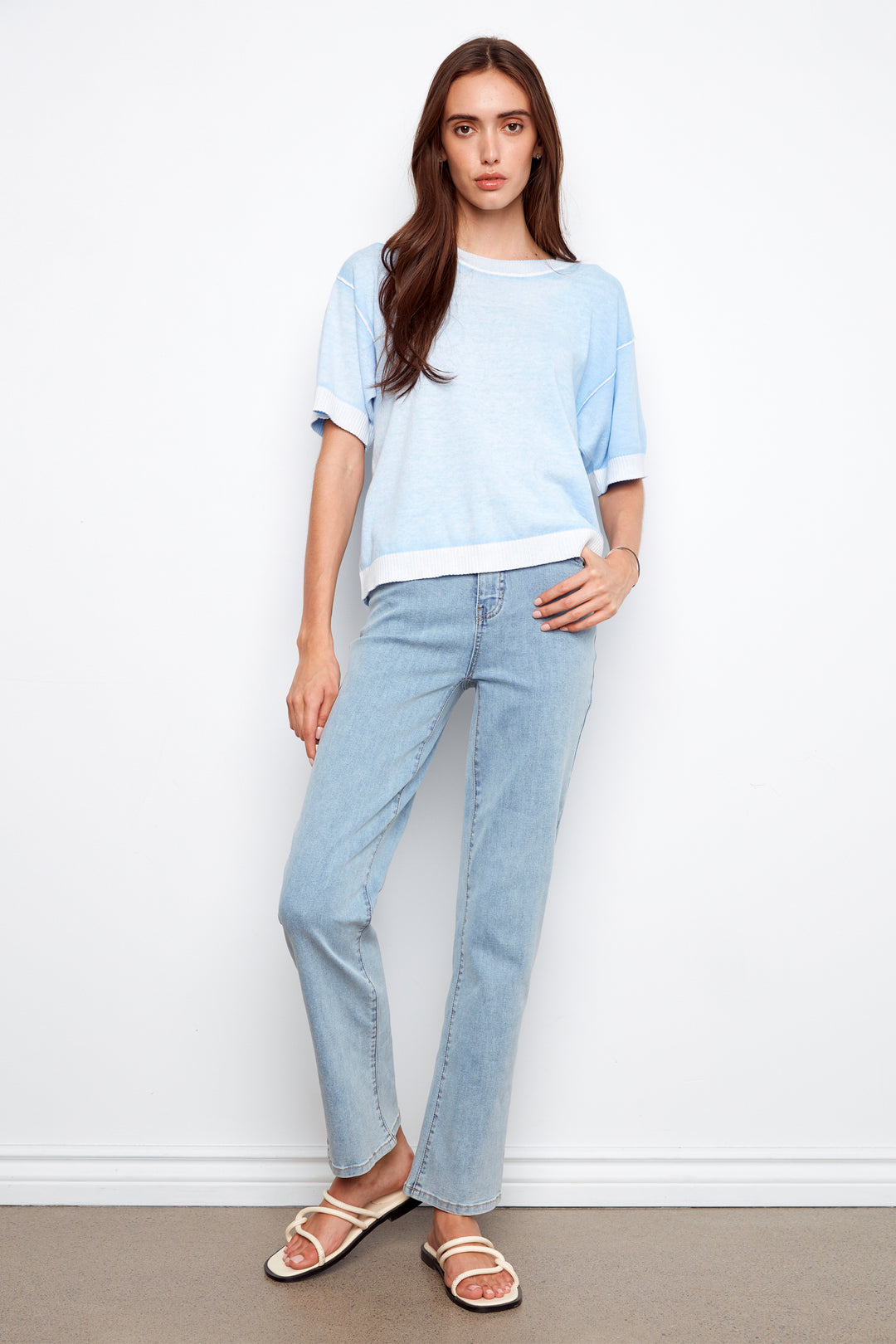 Woman wearing a light blue top and jeans against a white background