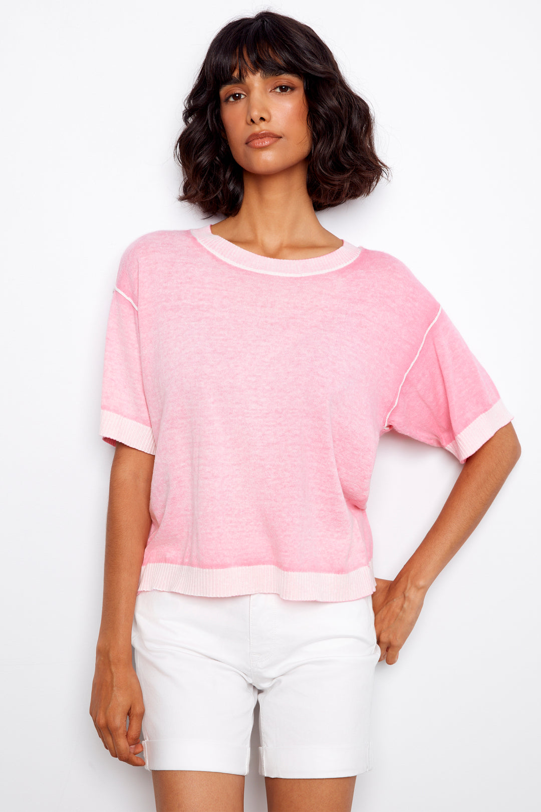 Woman wearing a pink sweater top and white shorts on a white background