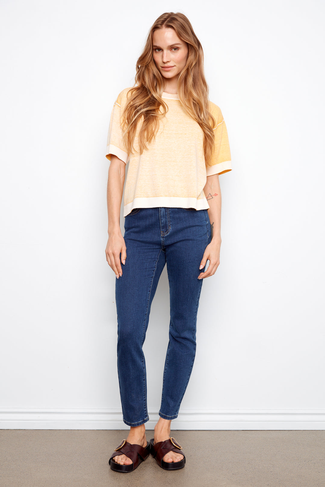 Woman wearing a yellow top and blue jeans against a white background