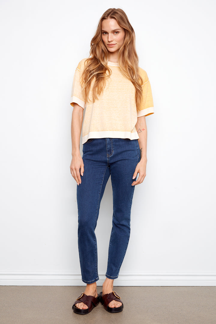 Woman wearing a yellow top and blue jeans against a white background