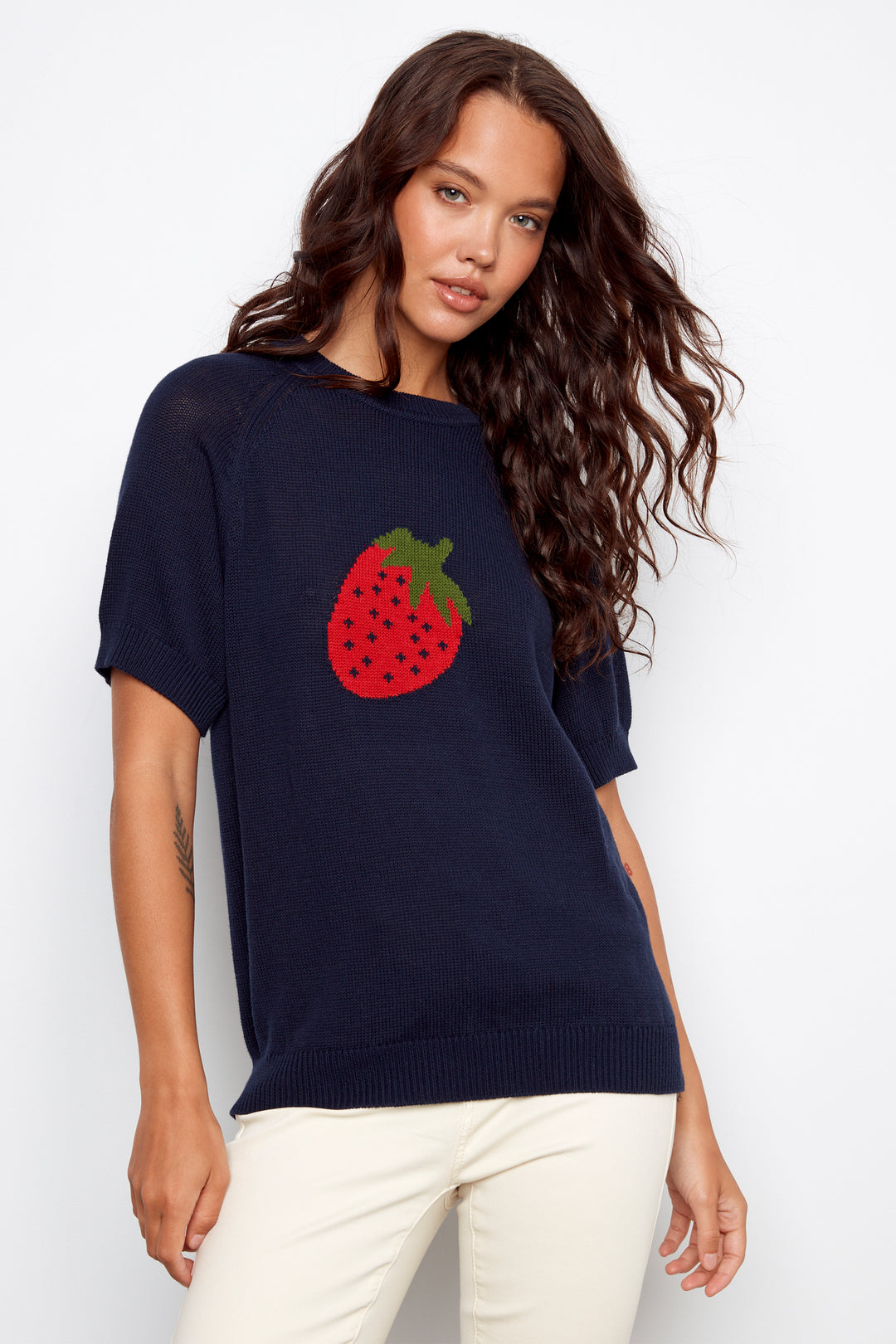 Woman wearing a navy sweater with a strawberry design on a white background