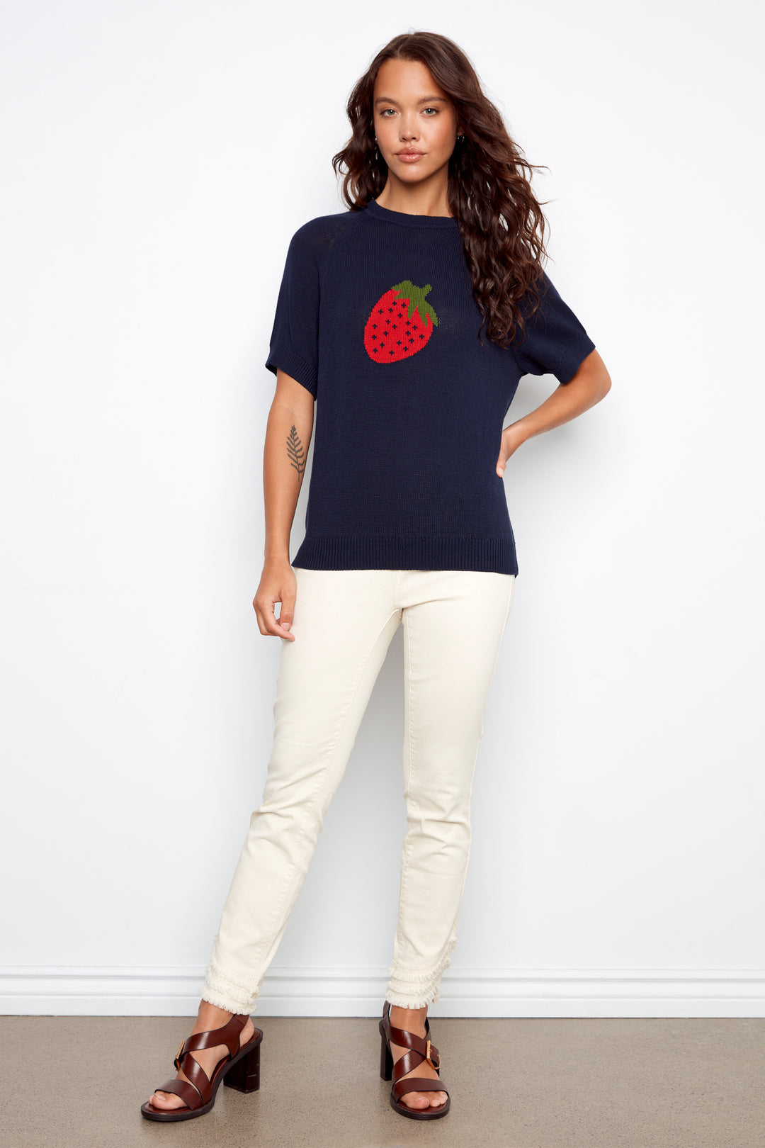 Woman wearing a navy blue t-shirt with a strawberry design and white pants against a white background
