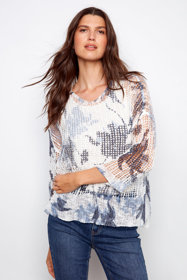 Woman wearing a patterned top and jeans against a white background