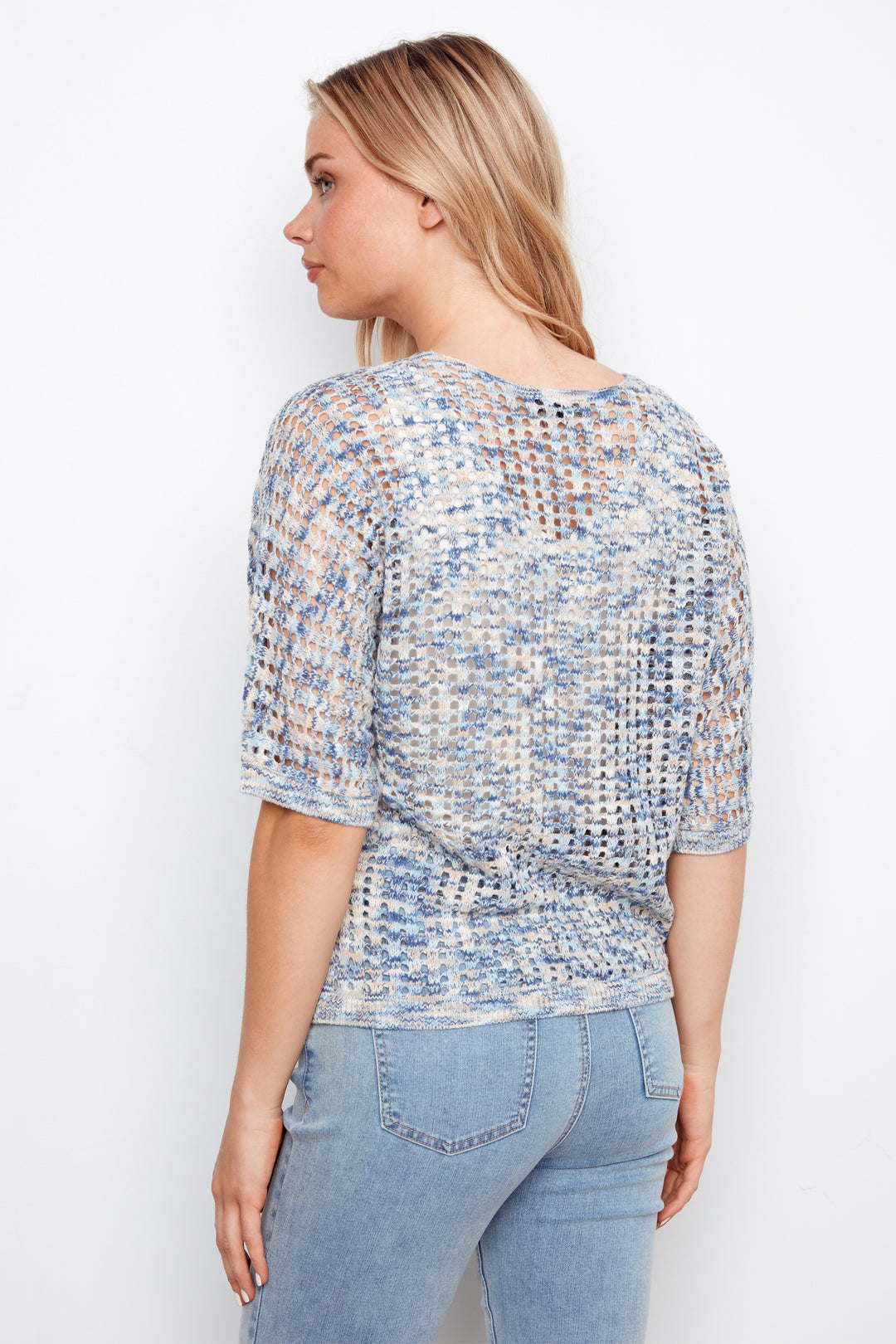 Woman wearing a patterned sweater top and jeans against a white background